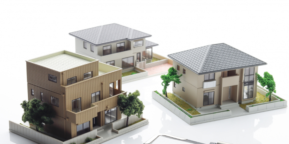 建築模型の住宅が3棟並び、手前にコンパスと鉛筆が置かれている様子