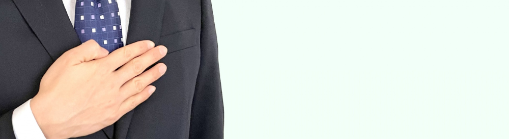 スーツ男性が胸に手を当て誓いを示す姿を左寄せで撮影。右側にテキスト配置可能な信頼・誠実イメージ