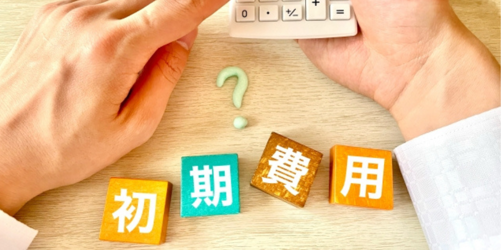 電卓を持つ手と「初期費用」の文字ブロック、中央にクエスチョンマークが置かれている画像