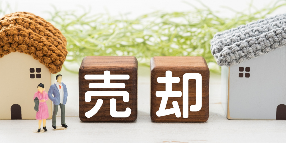 売却をイメージした木製ブロックと家の模型。夫婦のミニチュア付き
