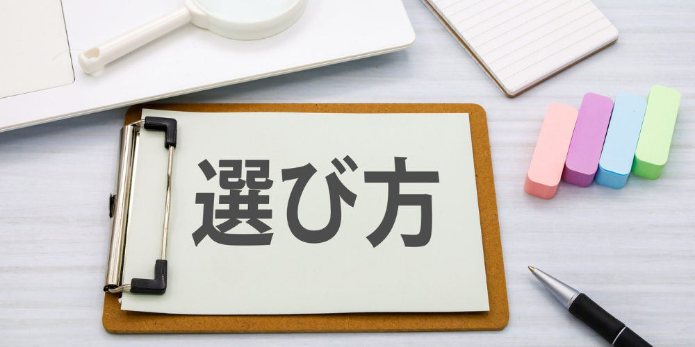 クリップボードに置かれた「選び方」のメモと、ノートや虫眼鏡が並ぶ作業机の様子