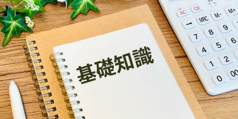 ノートに「基礎知識」と書かれ、電卓やペン、植物と一緒に机の上に置かれている画像