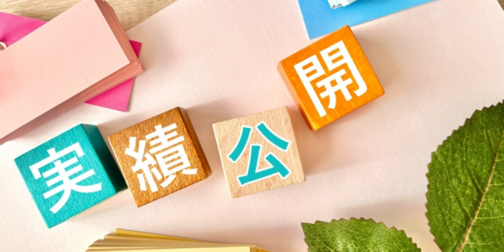 「実績公開」と書かれたカラフルな木製ブロックが並び、周囲に紙や葉が置かれている明るい雰囲気の構成