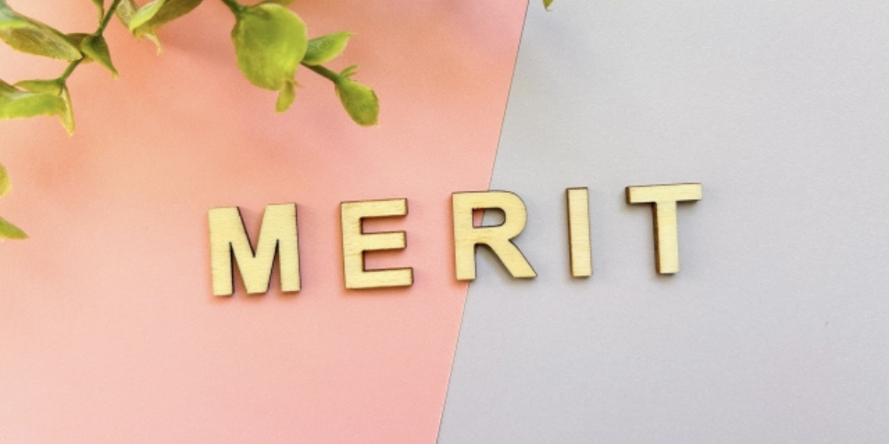 ピンクとグレーの背景の上に木製の文字で「MERIT」と並べられている