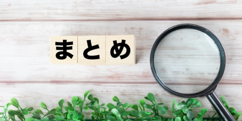 木目の背景に置かれた「まとめ」の文字ブロックと虫眼鏡、手前に観葉植物。