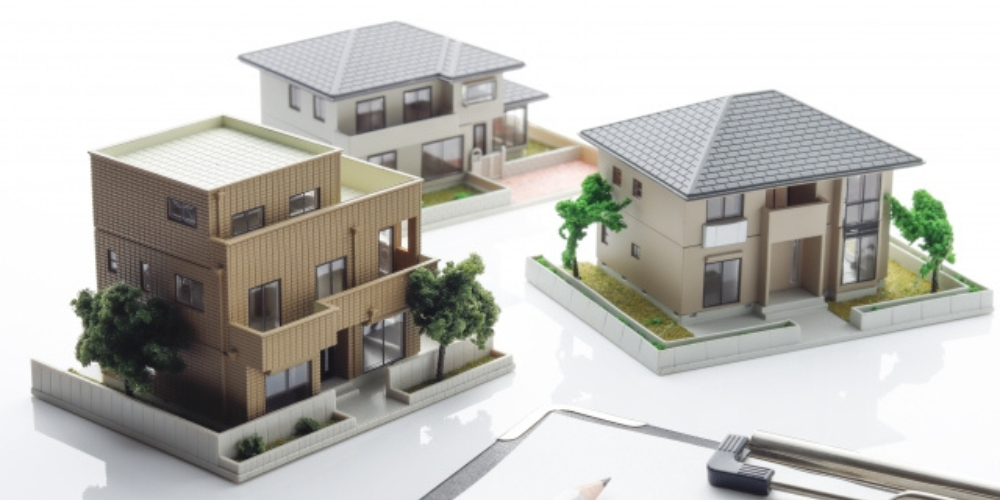 注文住宅のミニチュア模型が3棟並べられており、手前には設計図と定規が置かれている画像