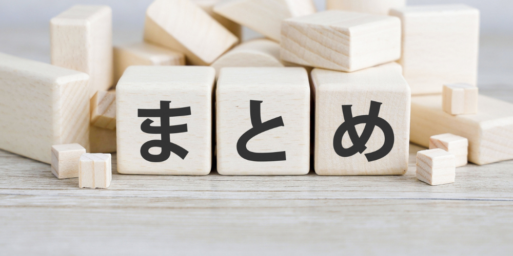 木製ブロックに「まとめ」の文字が書かれ、背景に積まれた木のブロックが広がる