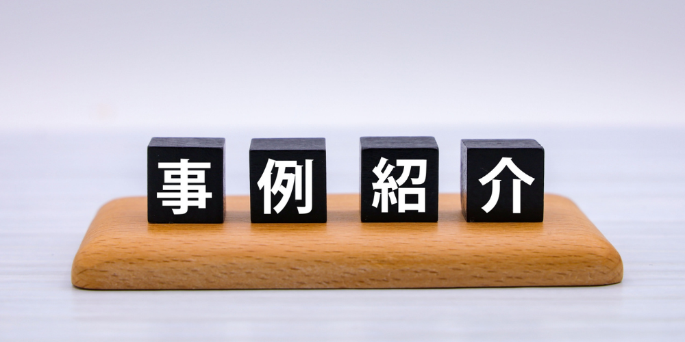 木製プレート上に黒いキューブ４個を並べ、白文字で「事例紹介」と示した実績紹介セクション用のビジュアル