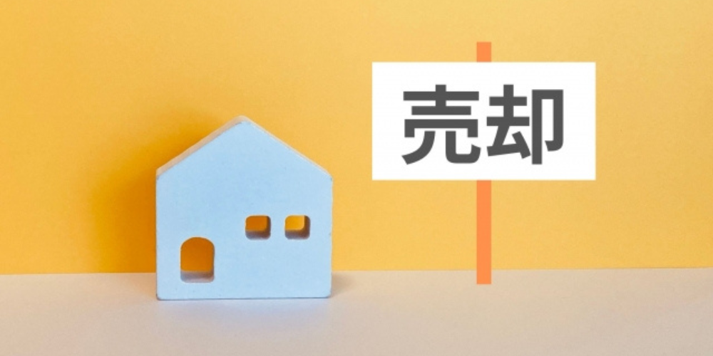 黄色い背景に青い家の模型と「売却」と書かれたプレートが配置されている画像