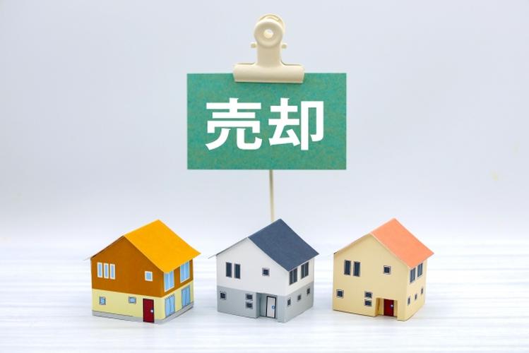 「売却」の文字と3軒のカラフルな家の模型が並ぶ、住宅の売却や不動産取引をイメージした写真