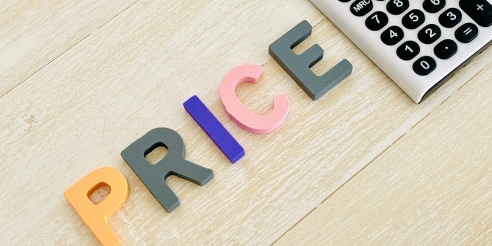 「“PRICE”のカラフルな文字と白い電卓が置かれた木目調のデスク」