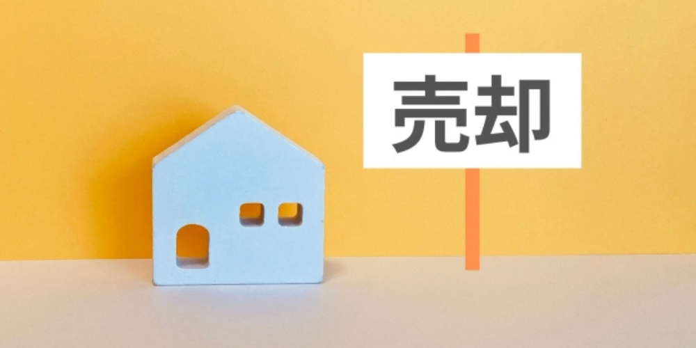 黄色と白の背景に青い家の模型と「売却」と書かれたプレートが並んでいる