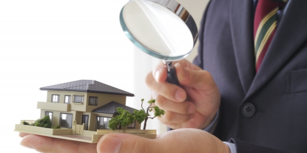 ビジネスマンが住宅模型を手に持ち、虫眼鏡でじっくり観察している画像