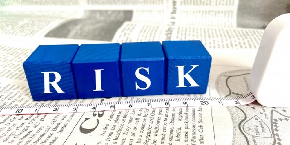「“RISK”の文字が書かれた青いブロックと新聞紙、巻き尺が並べられたイメージ」