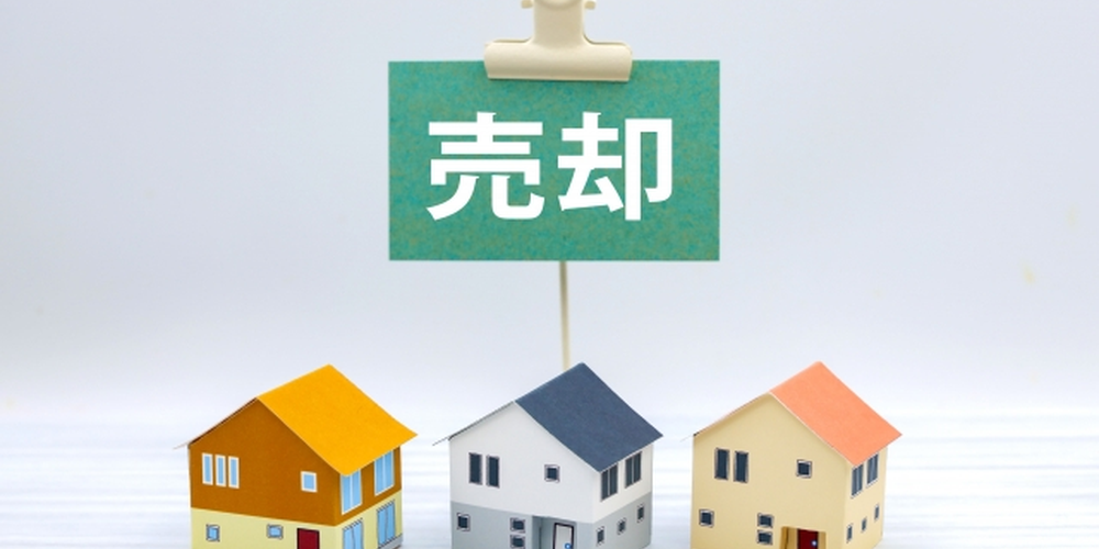 売却の札と並ぶ三軒の住宅模型、不動産売却をイメージした写真