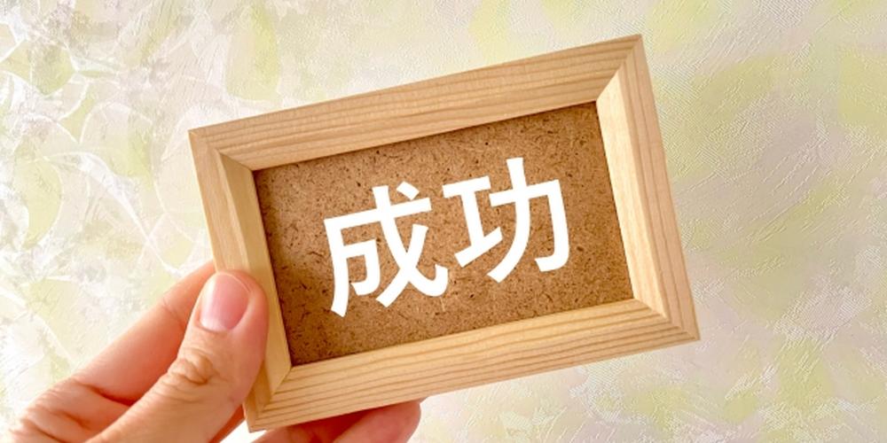 「“成功”の文字が書かれた小さな額縁を手に持つ様子」