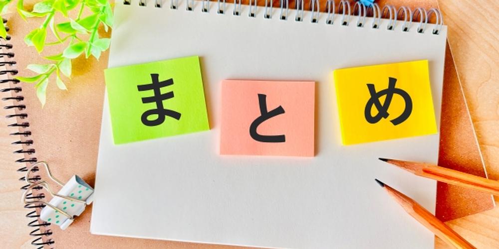 「“まとめ”の文字が書かれた付箋がノートに貼られ、文房具や観葉植物が彩るデスクの上」