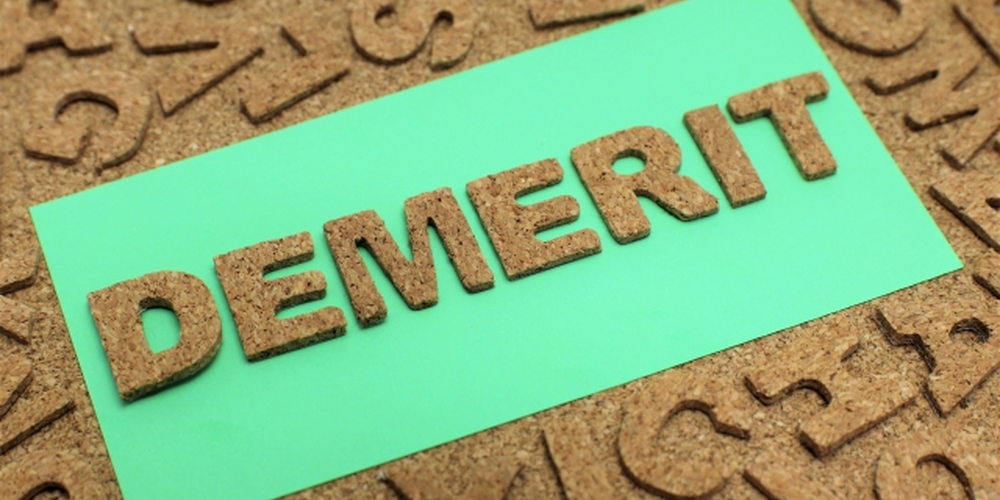 コルク素材の文字で『DEMERIT』と書かれた緑のカード、デメリットや注意点を示すイメージ