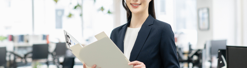 オフィス内でファイルを手に微笑むスーツ姿女性