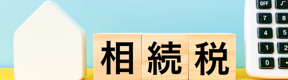 小さな家型オブジェと電卓の間に「相続税」と書かれた木製キューブを並べ、相続課税を連想させる構図