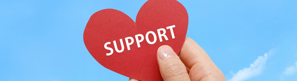 青空の下で「SUPPORT」と書かれた赤いハートを持つ手