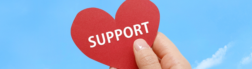 青空を背景に「SUPPORT」と書かれた赤いハートを持つ手