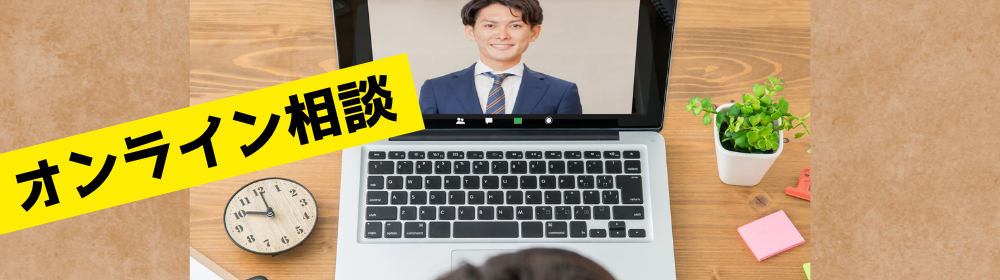 ノートPCの画面にスーツ姿の男性が映るビデオ通話と、黄色帯に黒文字で「オンライン相談」と表示されたバナー。机上には時計や観葉植物、ペンなどが並ぶ