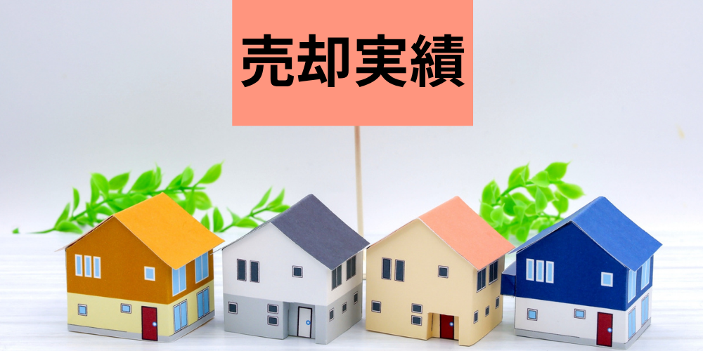 テーブル上にカラフルな紙製住宅模型を４棟並べ、背後のピンクのフラッグに黒文字で「売却実績」と示した実績紹介画像