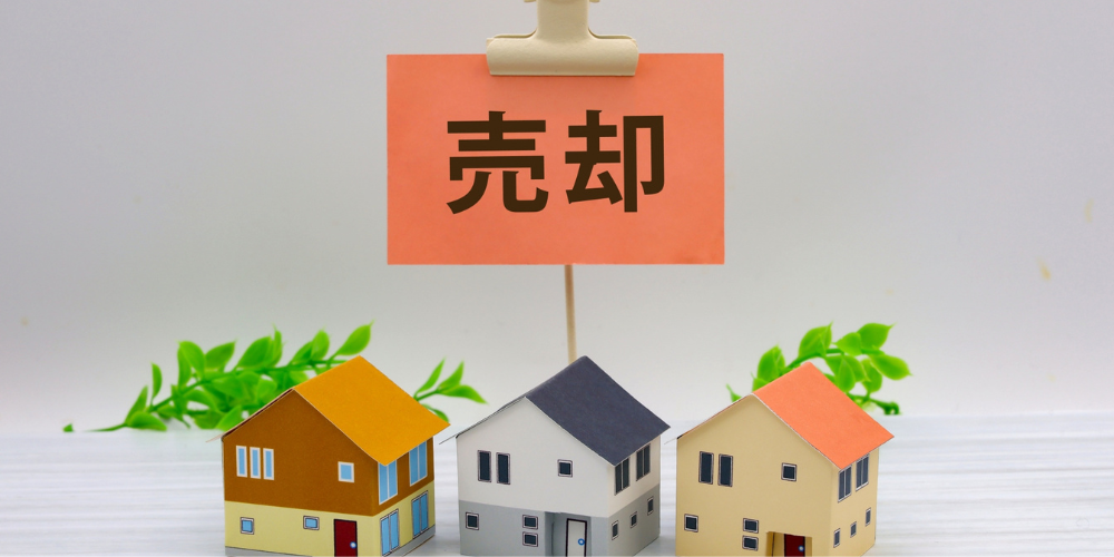 ミニチュア住宅と「売却」札を掲げるシーン