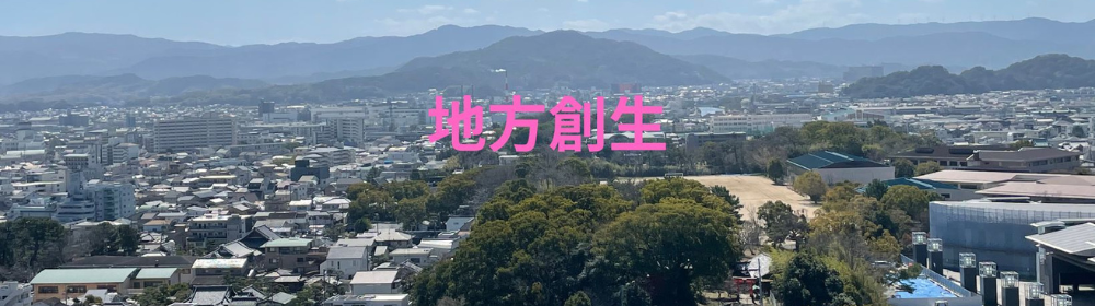 山に囲まれた住宅密集地を高所から撮影し、中央にピンク色で「地方創生」と表示